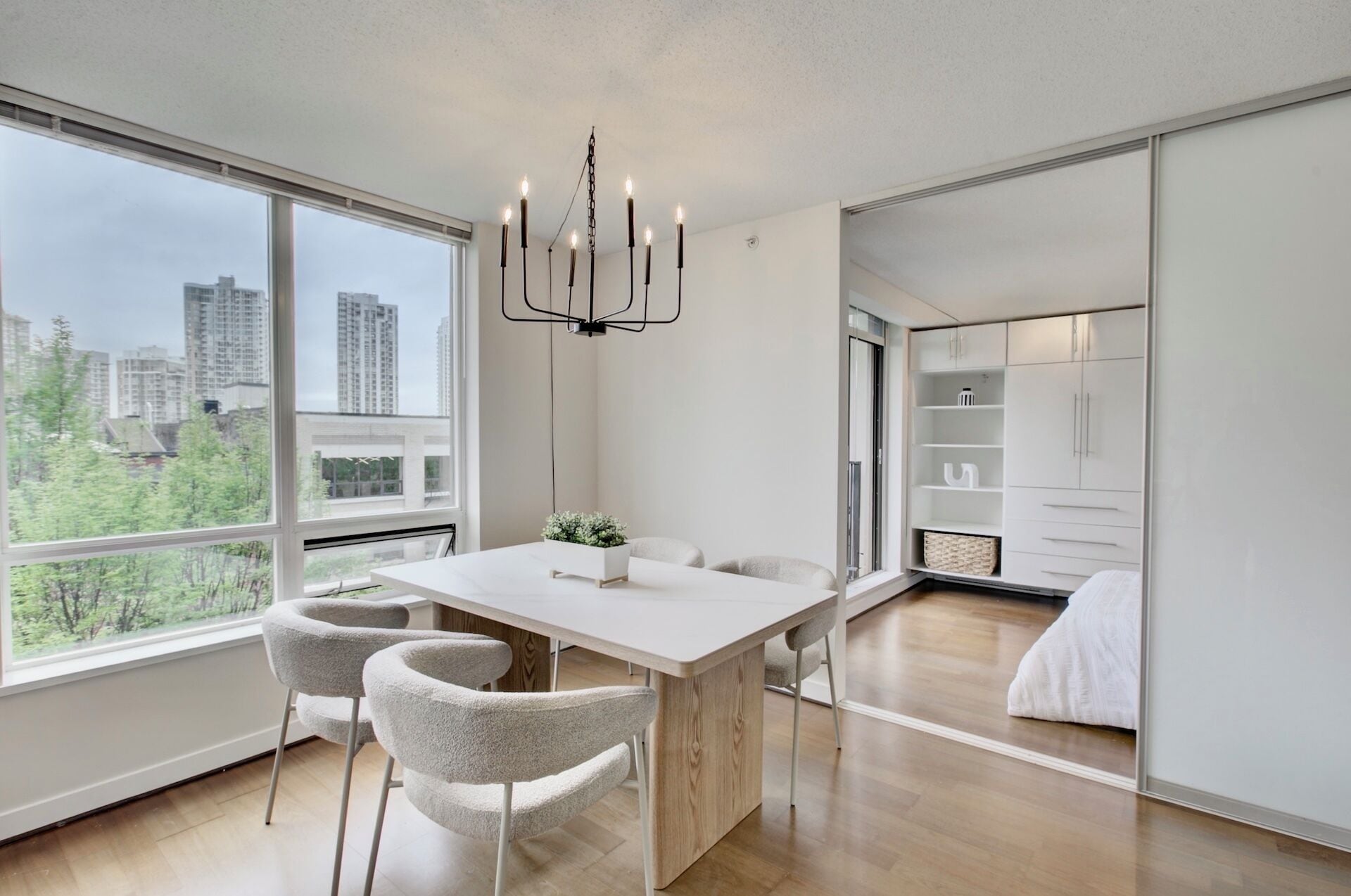 A modern interior with a dining area, a large window with a city view, and a walk-in closet.