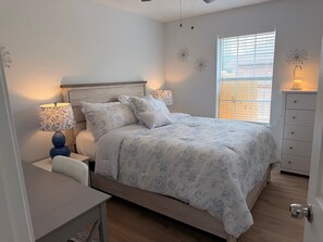 Ein Schlafzimmer mit Bett, Nachttischlampen, einem Nachttisch, einem Schminktisch und einem Fenster mit Jalousien.
