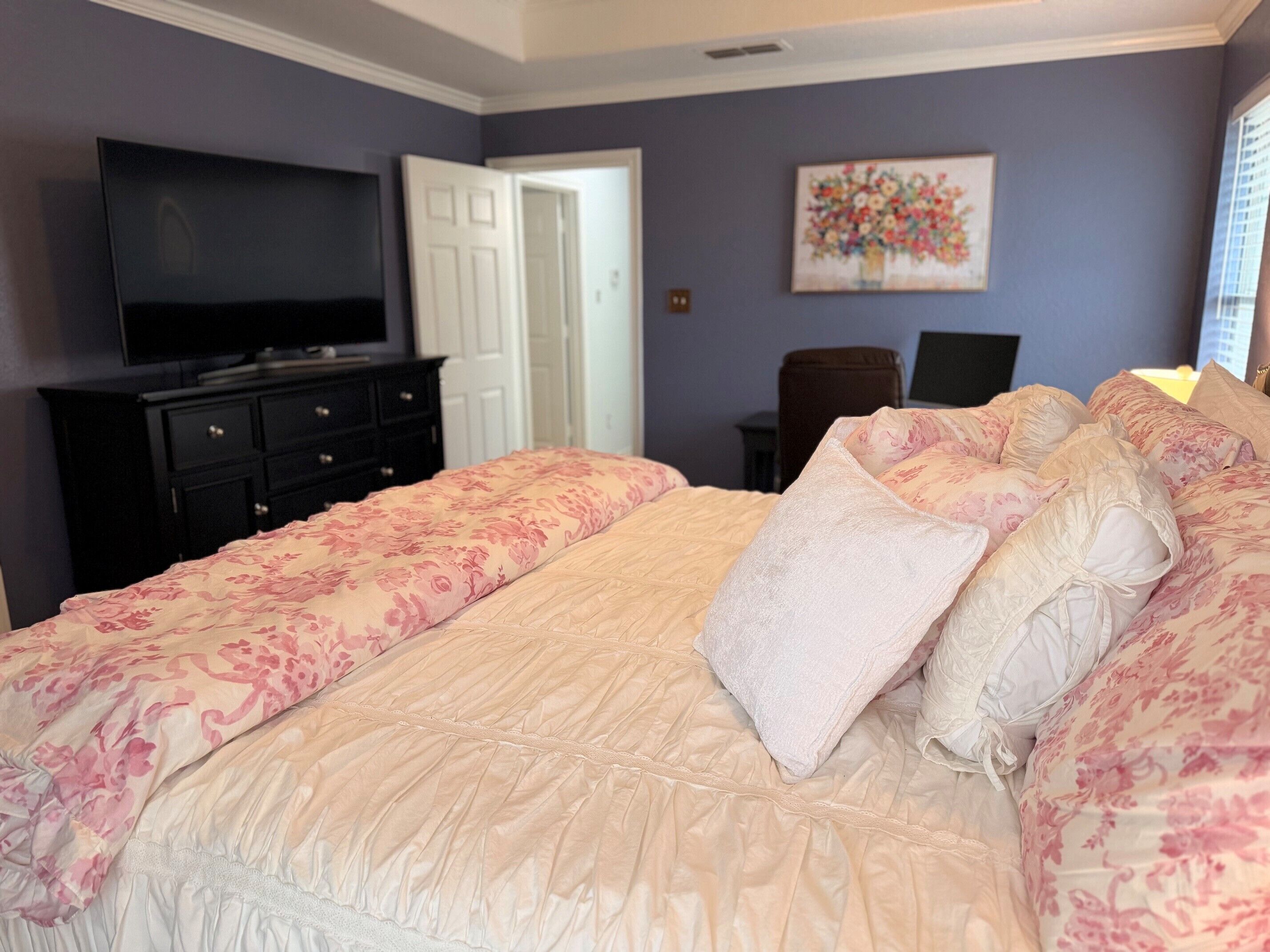 A bedroom with a large bed, a television, a desk, and a chair.