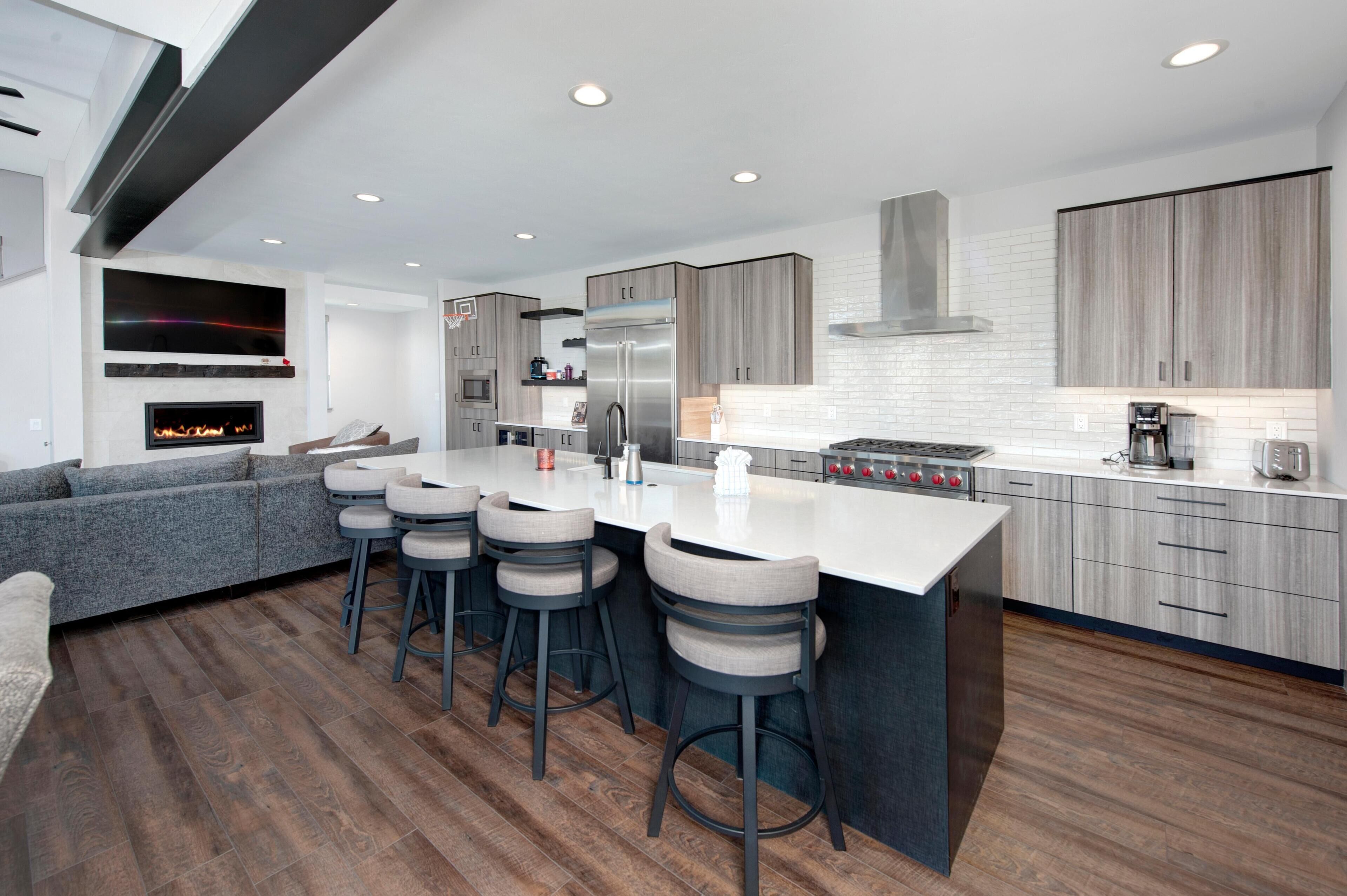 A modern kitchen with a central island, bar stools, a built-in oven, and a large refrigerator.