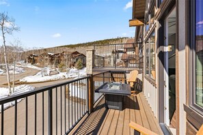 Eine Holzterrasse mit Tisch und Stühlen, eine Glastür und Blick auf andere Gebäude.