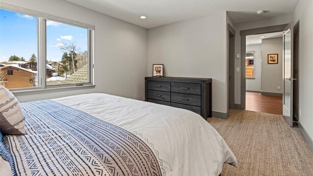 Een slaapkamer met een groot raam, een bed, een dressoir en een gang naar een andere kamer.