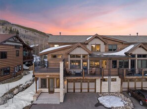 Un chalet à étages doté d’une façade en pierre, de balcons en bois et offrant une vue sur un paysage enneigé.