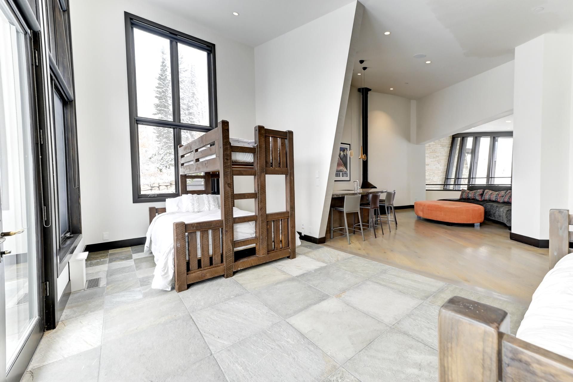 A modern bedroom with a bunk bed, a dining area with a table and chairs, and a large window with a view of trees.