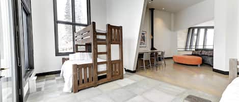 A modern bedroom with a bunk bed, a dining area with a table and chairs, and a large window with a view of trees.