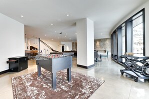 Una sala de estar moderna con mesa de fútbol de mesa, bicicleta estática y zona de cocina al fondo.