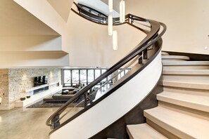 A modern spiral staircase with a minimalist design, a stone accent wall, and a seating area with a fireplace. - KBM Resorts| Walk to Slopes, Sports Court, Private Home Theater, Sleeps 17, Outdoor Hot Tub PCO-184M (Park City)