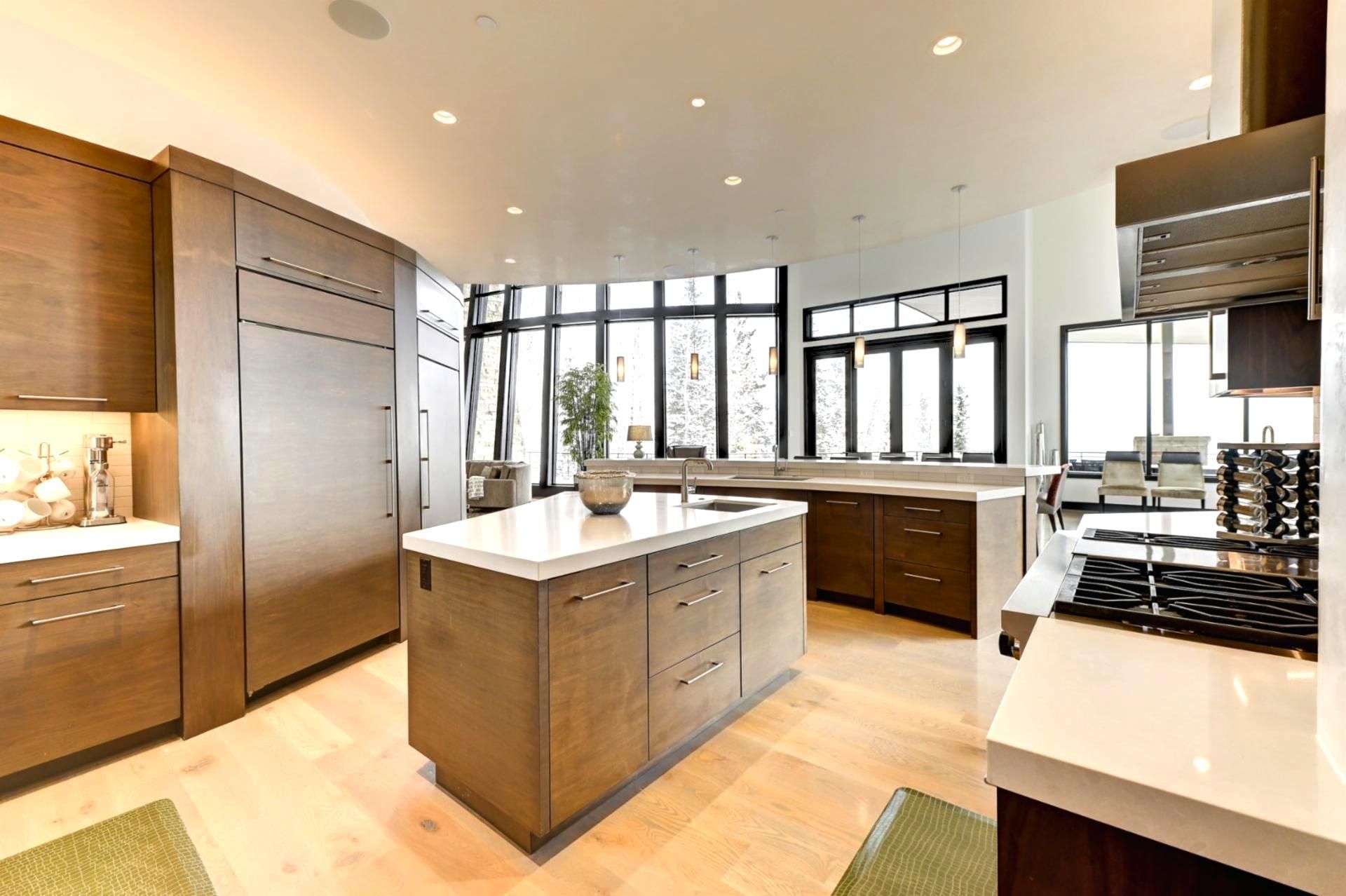 A modern kitchen with a central island, wooden cabinets, and large windows.