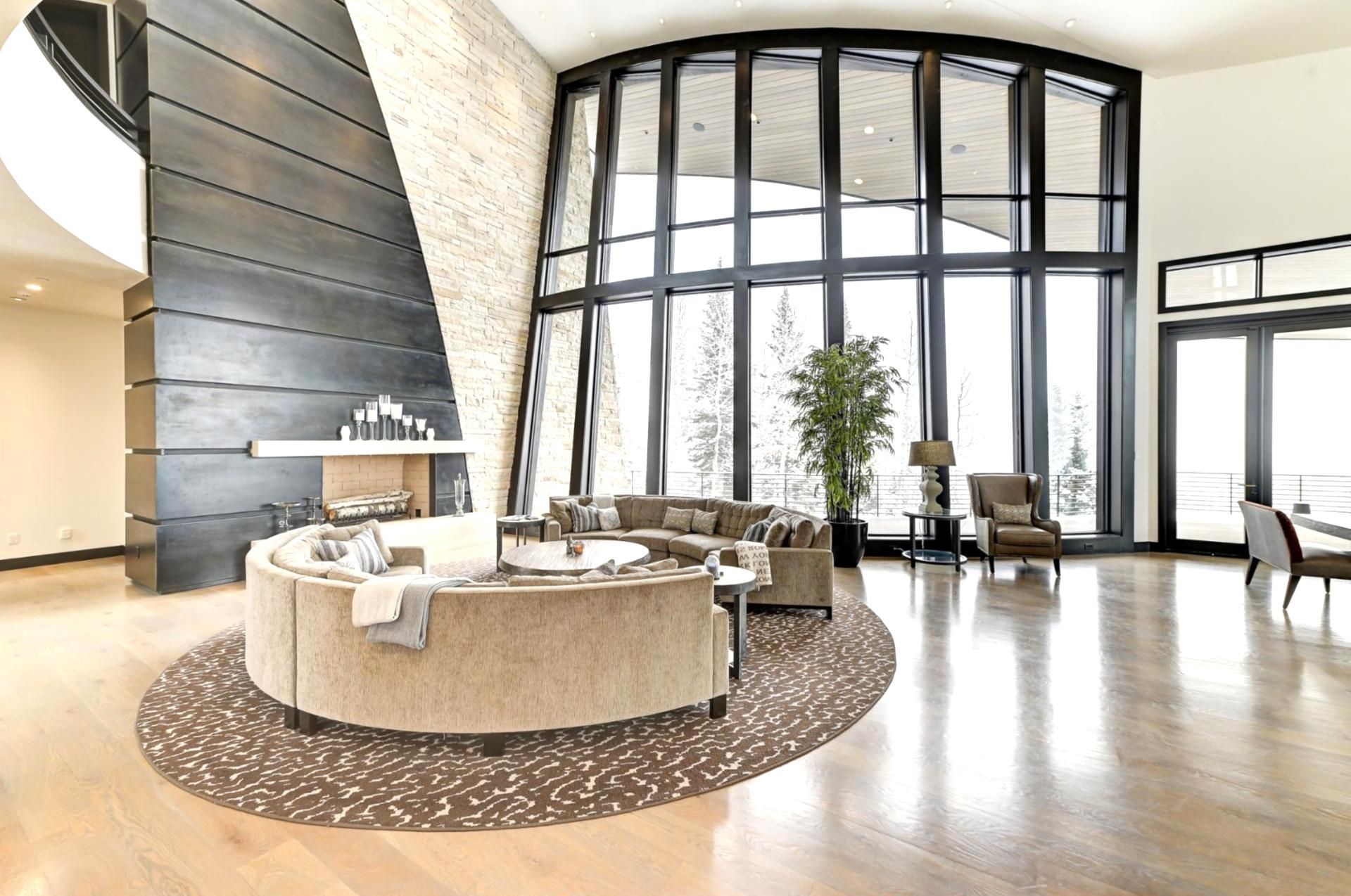 A spacious living area with a large fireplace, a curved seating arrangement, and large windows offering a view of the outdoors.