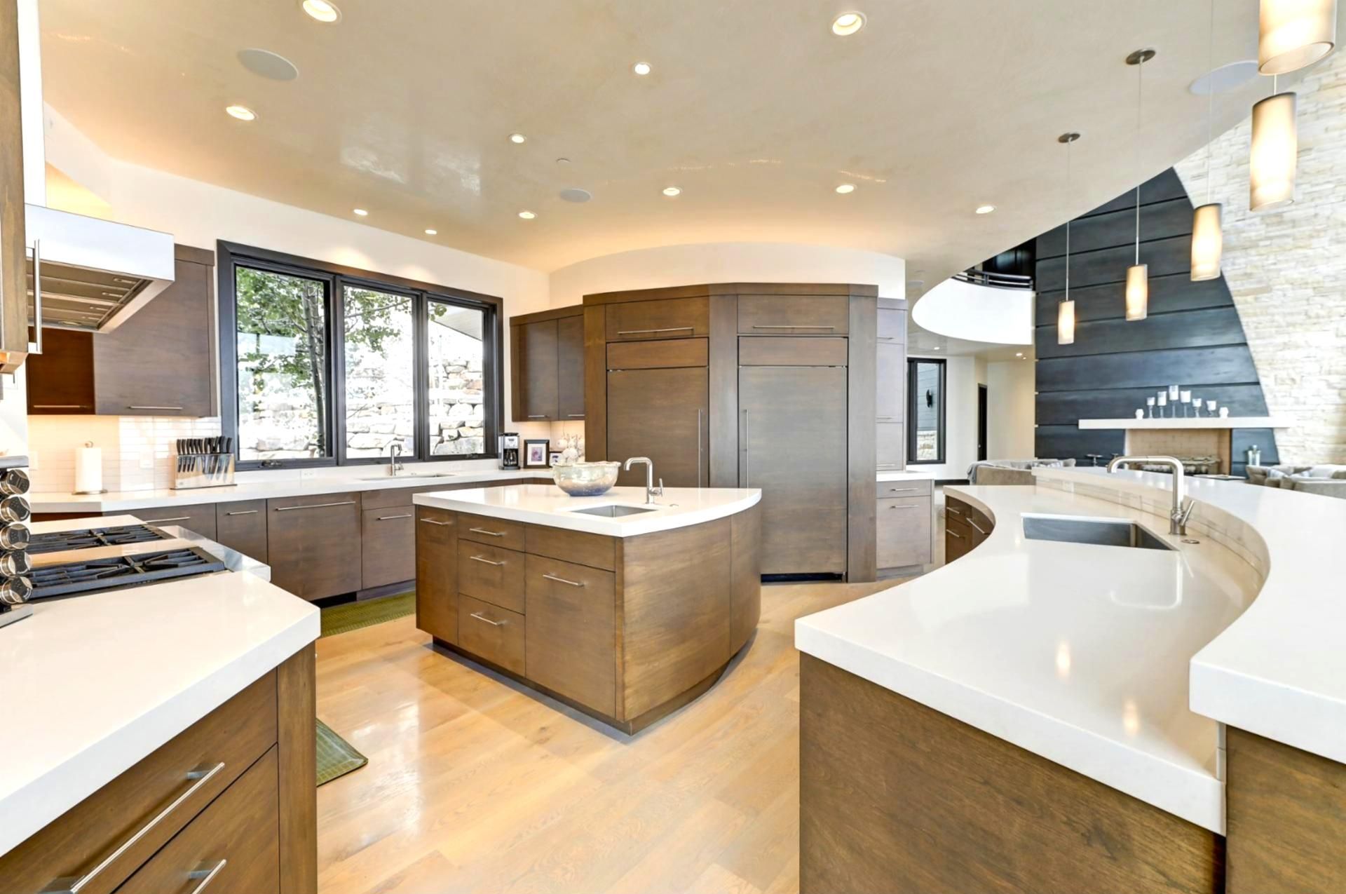 Een moderne keuken met een centraal eiland, inbouwapparatuur en een groot raam dat voor natuurlijk licht zorgt.