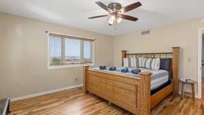 Un dormitorio con cama de madera, ventilador de techo, ventana con persianas y vistas al exterior.