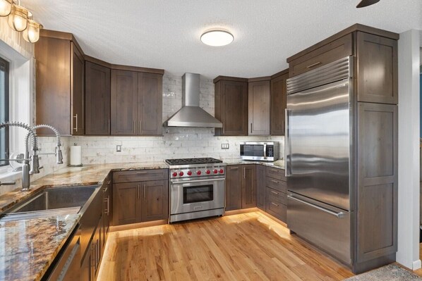 A kitchen with dark wooden cabinets, stainless steel appliances, a marble countertop, and a wooden floor.