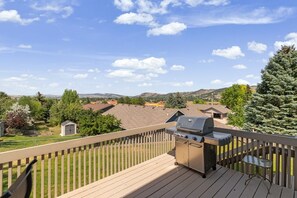 A deck with a barbecue grill, a small table, and a view of a residential area with houses and trees.