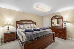 A bedroom with a wooden bed, two bedside tables with lamps, a dresser, and a large mirror.