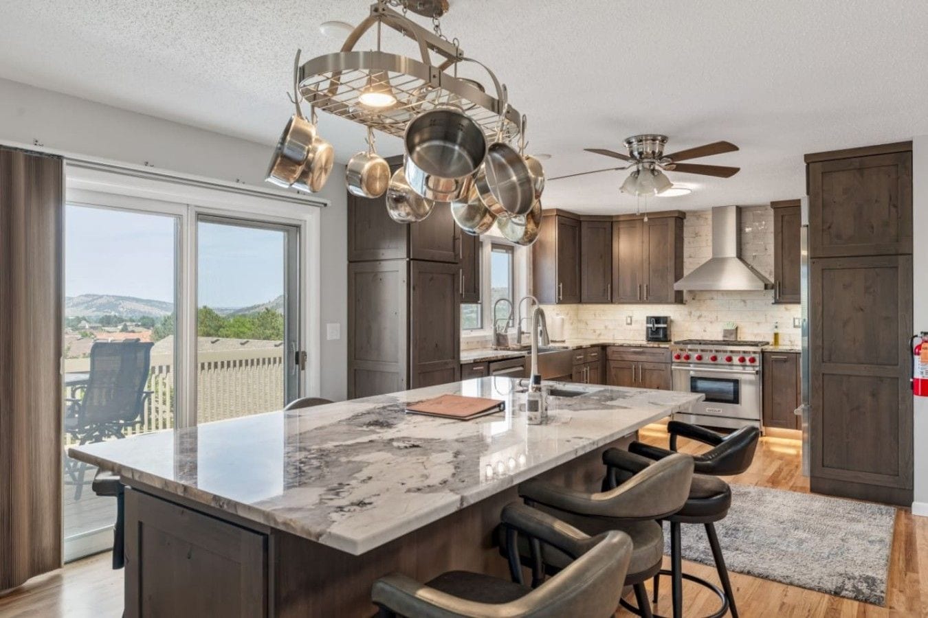 A modern kitchen with a large island, dark wood cabinets, a stainless steel stove, and a view of the outdoors.
