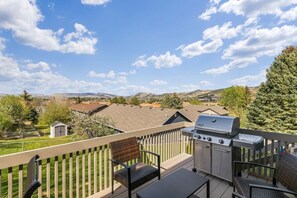 A balcony with a grill, seating, and a view of a residential area.