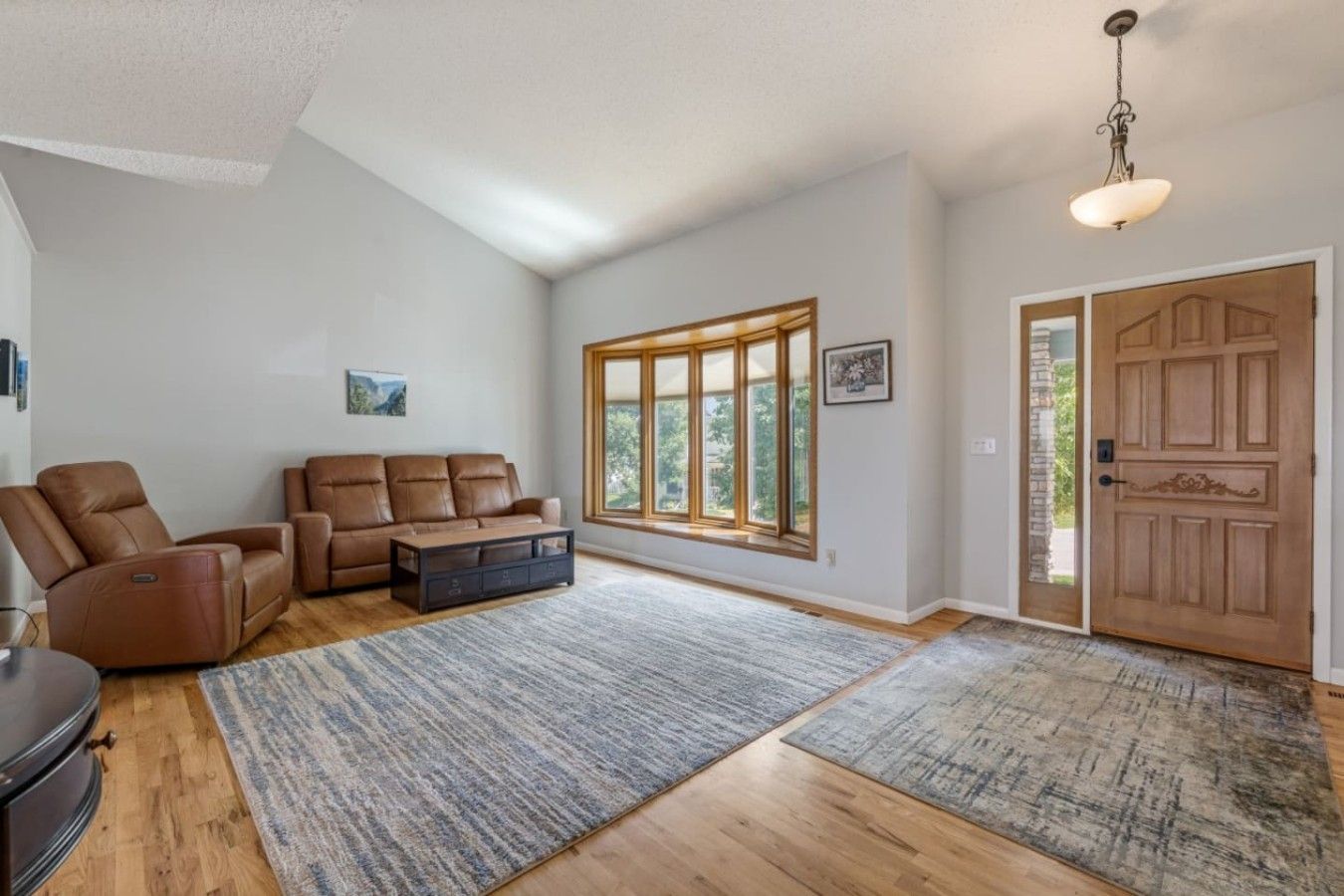 A spacious living room with a leather sofa, a recliner, and a coffee table. There is a large window providing a view of the outdoors.