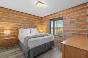 A bedroom with a bed, bedside tables, and a view through a window. - Log cabin on a canyon, panoramic hills, 3 levels (Rapid City)