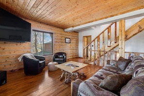 A log cabin interior with a wooden floor, a sofa, a chair, a coffee table, and a staircase. - Log cabin on a canyon, panoramic hills, 3 levels (Rapid City)