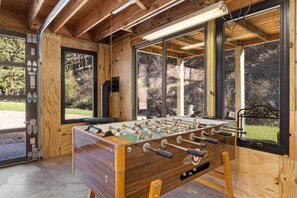 A wooden-floored room with a foosball table, large windows, and a view of the outdoors. - Creekside Retreat | Fireplace + Gameroom (Rapid City)