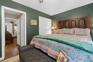 A bedroom with a bed, a nightstand, a lamp, a door, and a painting on the wall. - Creekside Retreat | Fireplace + Gameroom (Rapid City)