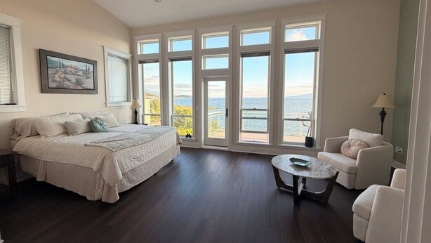Amplia habitación con una cama grande, un sofá, una mesita redonda y vistas al mar a través de amplias ventanas.