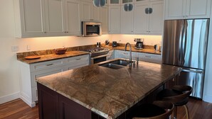 Una cocina moderna con armarios blancos, un refrigerador de acero inoxidable, una isla de mármol y un horno empotrado.