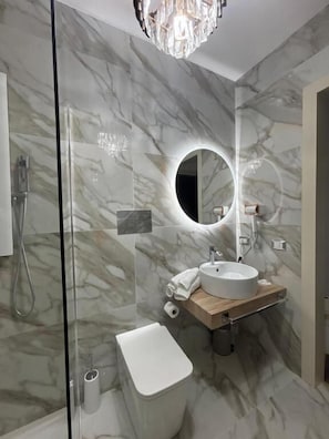 Ein modernes Badezimmer mit Marmorwand, rundem Spiegel, Waschbecken und Toilette.
