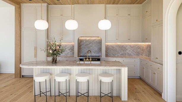 Une cuisine dotée d’un îlot en marbre, de tabourets de bar, de luminaires suspendus et d’un plafond en bois.
