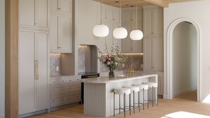 Une cuisine moderne avec des meubles blancs, un îlot central doté de tabourets, des luminaires suspendus et un pare-feu en marbre.