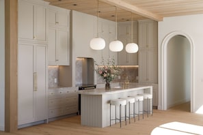 Eine moderne Küche mit weißen Schränken, einer zentralen Kochinsel mit Barhocker, Pendelleuchten und einer Marmor-Spritzschutzwand.