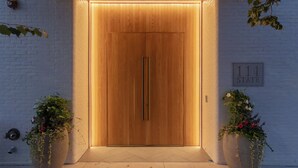 Une porte en bois avec une plaque portant un numéro, deux grands jardinières remplies de fleurs et un mur en briques blanches.