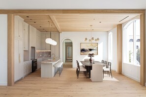Eine moderne Küche mit Holzbalken, einem Essbereich mit rundem Tisch und großen Fenstern.