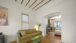 A living room with a sofa, a coffee table, a piano, and a bed in the background. - Charming Character-filled Heritage Home near DT (Vancouver)