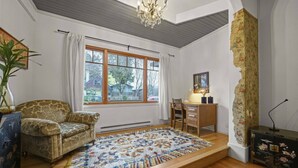 A room with a wooden floor, a patterned rug, a chair, a desk with a lamp, a window with curtains, and a plant. - Charming Character-filled Heritage Home near DT (Vancouver)
