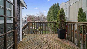 A wooden deck with a railing, a potted plant, and a view of surrounding buildings. - Charming Character-filled Heritage Home near DT (Vancouver)