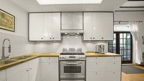 A modern kitchen with white cabinets, stainless steel appliances, and a wooden countertop. - Charming Character-filled Heritage Home near DT (Vancouver)
