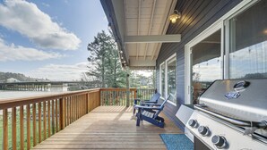 Une terrasse en bois avec un barbecue et deux chaises, donnant sur un quai et des arbres.