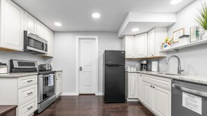 A modern kitchen with white cabinetry, a black refrigerator, a microwave, and a coffee maker.