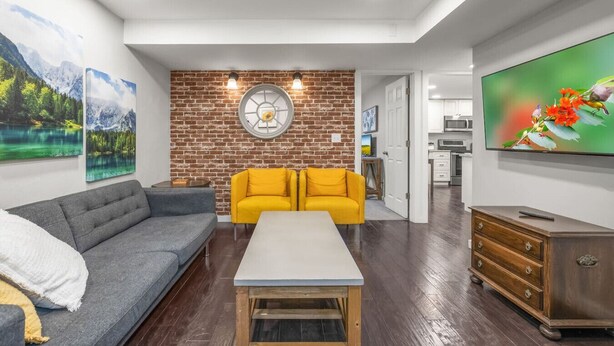 A living room with a sofa, a coffee table, a TV, and a brick wall.