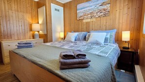 A wooden-paneled room with a bed, two bedside tables, a nightstand, and a painting on the wall.