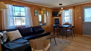 A cozy room with a sofa, a dining table with chairs, wooden walls, and a television.