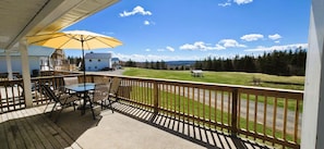 A covered outdoor area with a table and chairs, a yellow umbrella, and a view of a grassy field and trees.