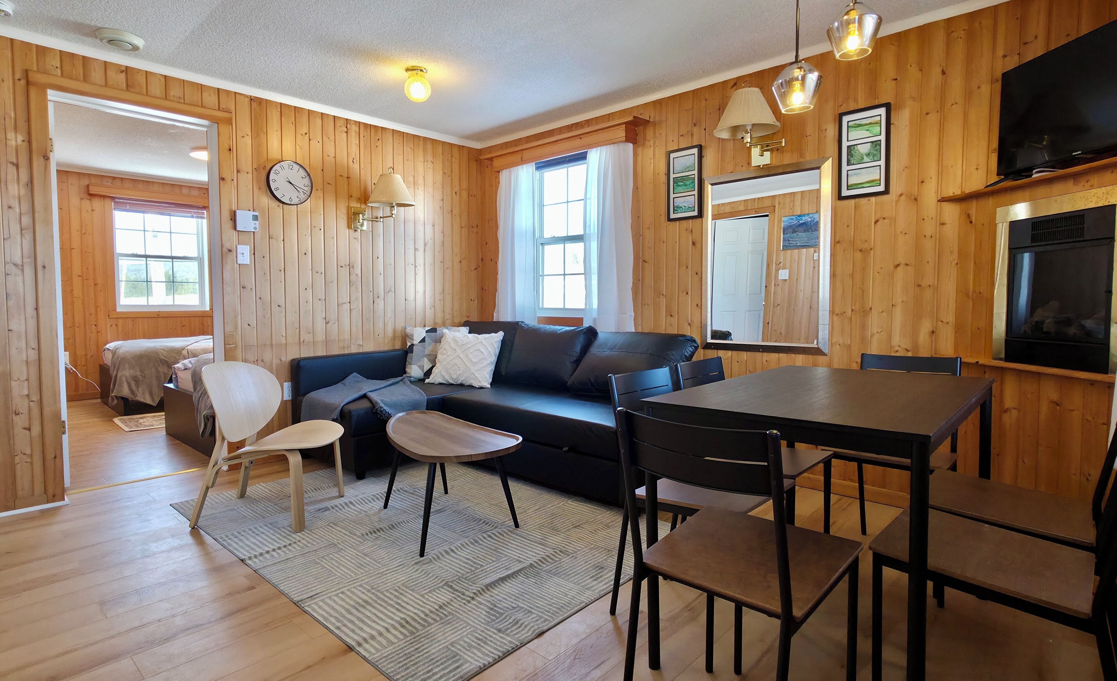 A wooden-paneled room with a sofa, a dining table, chairs, a TV, and a fireplace.