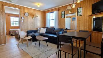 A wooden-paneled room with a sofa, a dining table, chairs, a TV, and a fireplace.