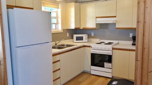 A compact kitchen with a refrigerator, microwave, stove, sink, and wooden flooring.