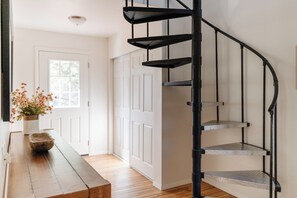 Eine Wendeltreppe mit Metallgeländer, ein Holztisch mit Blumenvase und eine weiße Tür mit Fenster.