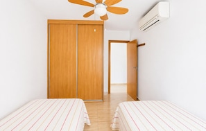 Una habitación con dos camas, un armario de madera, un ventilador de techo y un aire acondicionado.