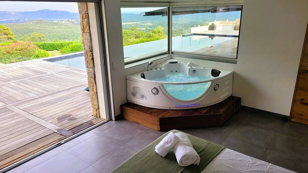 Une salle de bain moderne avec un jacuzzi, une vue sur une piscine et un paysage, et un lit avec des serviettes.