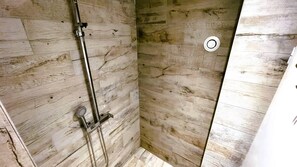 Eine Dusche mit einer Holzwand, einem Metall-Duschkopf und einem runden Lüftungsgitter.
